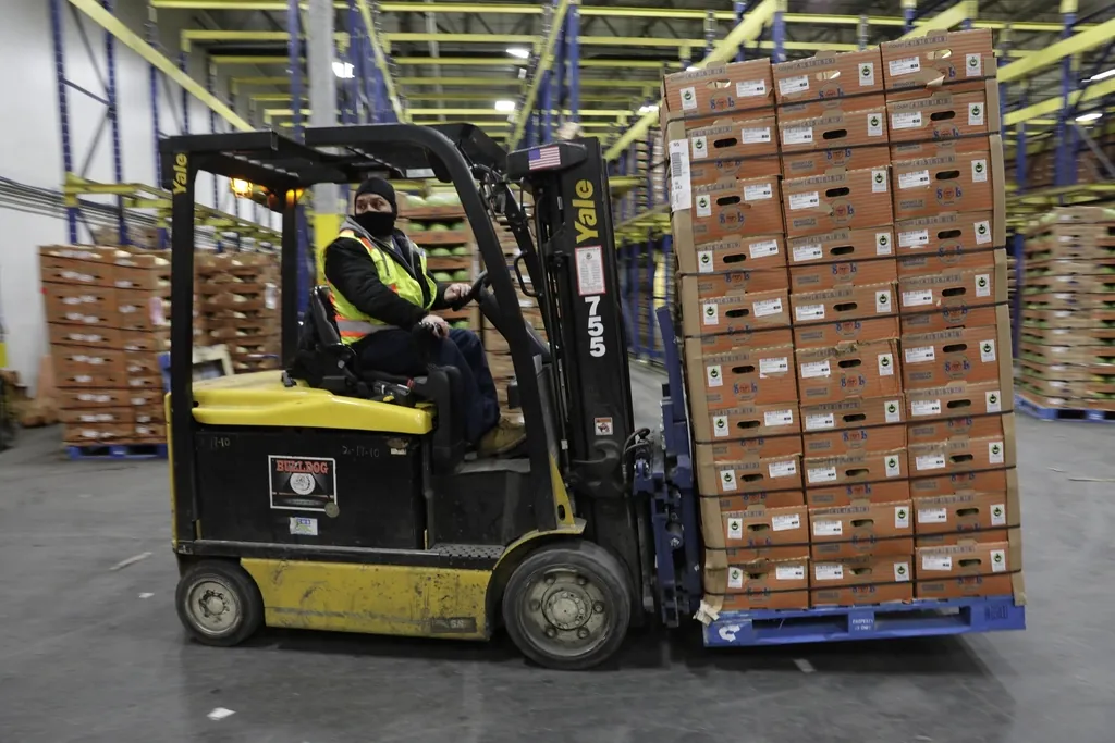 A forklift carrying a loaded pallet across a warehouse floor